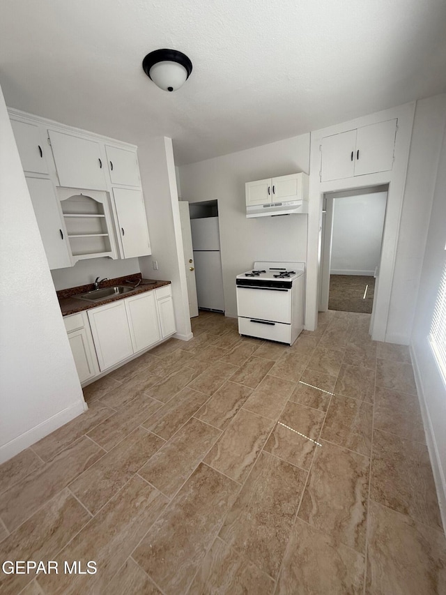 kitchen featuring white range with gas cooktop, open shelves, a sink, white cabinets, and dark countertops