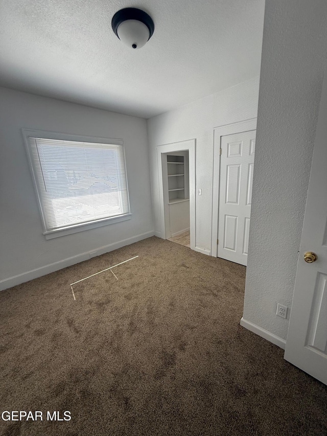 unfurnished bedroom featuring a textured wall, baseboards, carpet, and a textured ceiling