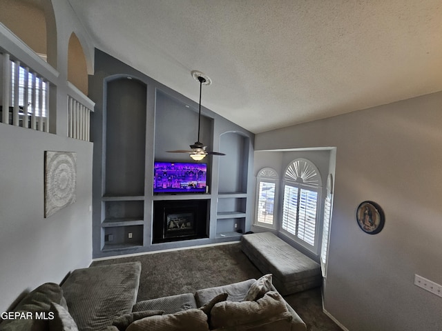 carpeted living area with built in shelves, a ceiling fan, a fireplace, vaulted ceiling, and a textured ceiling