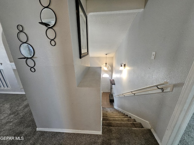 stairway featuring baseboards, carpet floors, and a textured wall