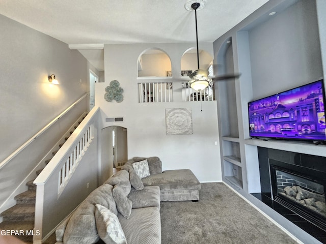 living area featuring built in shelves, a ceiling fan, visible vents, a glass covered fireplace, and carpet flooring