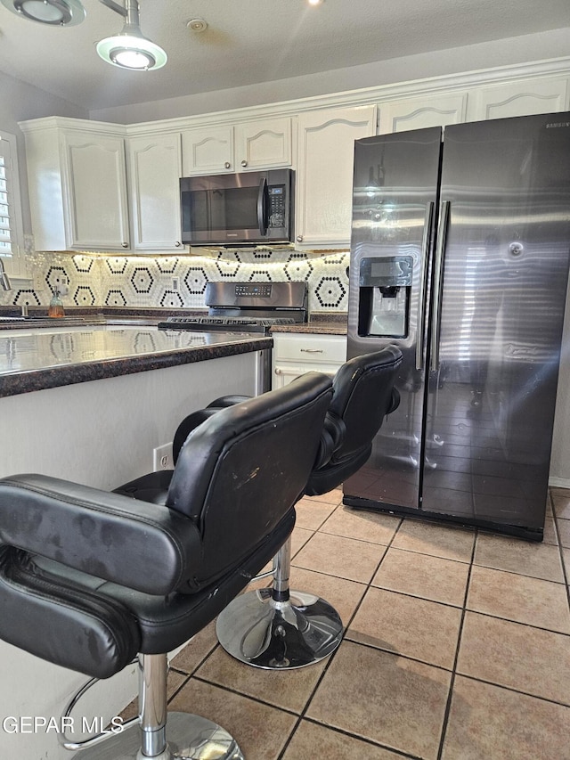 kitchen featuring fridge with ice dispenser, stainless steel gas stove, light tile patterned flooring, white cabinets, and decorative backsplash