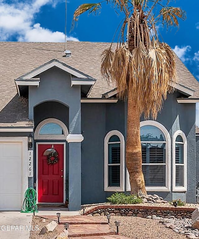 doorway to property with stucco siding, an attached garage, and a shingled roof