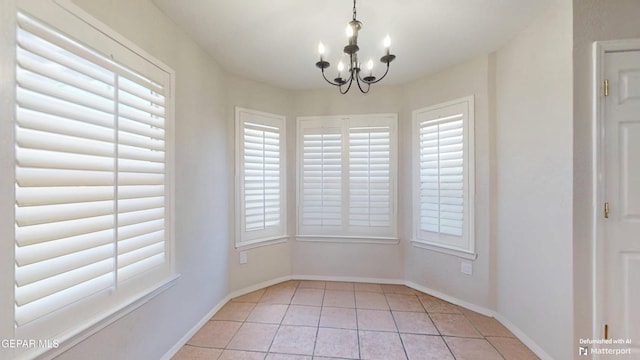 unfurnished dining area with light tile patterned flooring, a notable chandelier, and baseboards