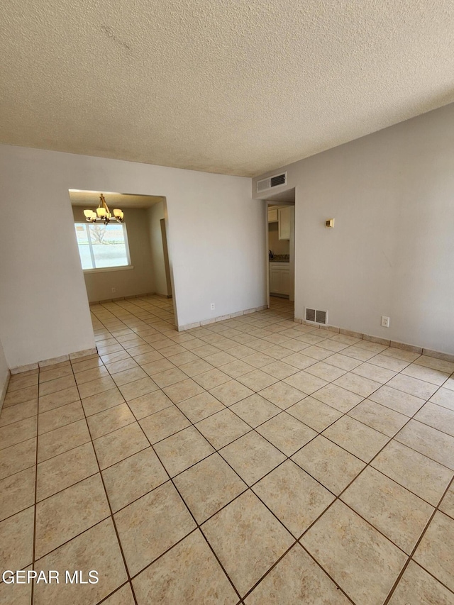 unfurnished room with a notable chandelier, visible vents, light tile patterned floors, and a textured ceiling