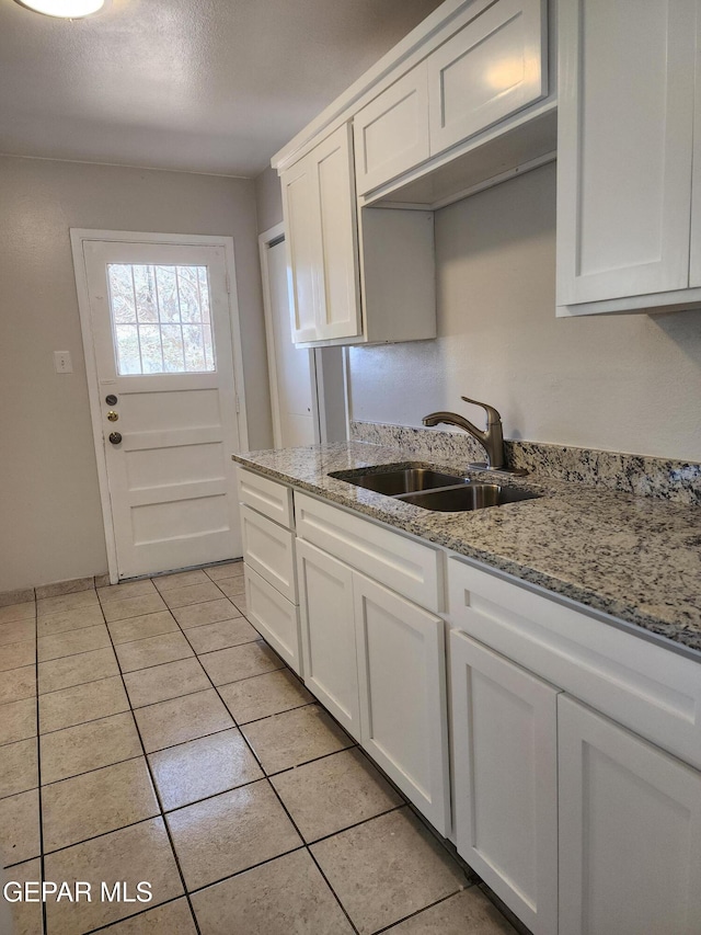 kitchen with light stone counters, white cabinets, light tile patterned flooring, and a sink