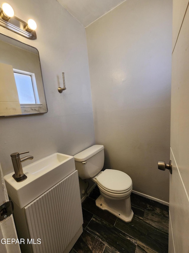 half bathroom featuring baseboards, toilet, wood finished floors, and vanity