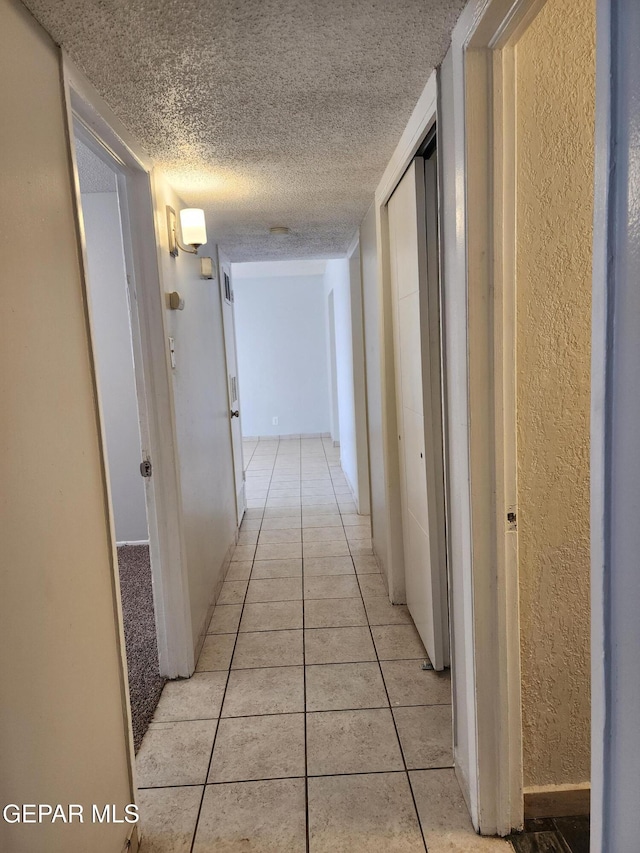 hall with light tile patterned floors, a textured ceiling, and a textured wall