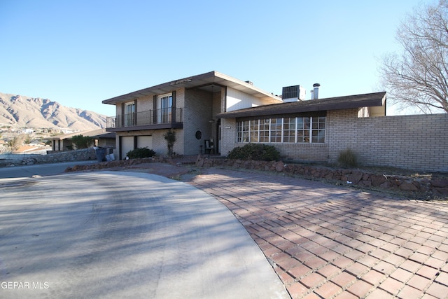 view of front of house with brick siding, an attached garage, central AC, a balcony, and a mountain view