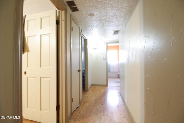 corridor with visible vents, baseboards, a textured ceiling, and light wood-style flooring