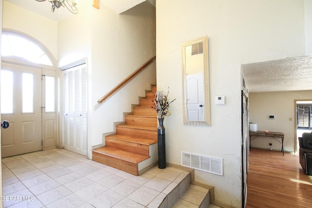 foyer with stairs, light wood-style floors, visible vents, and a textured ceiling