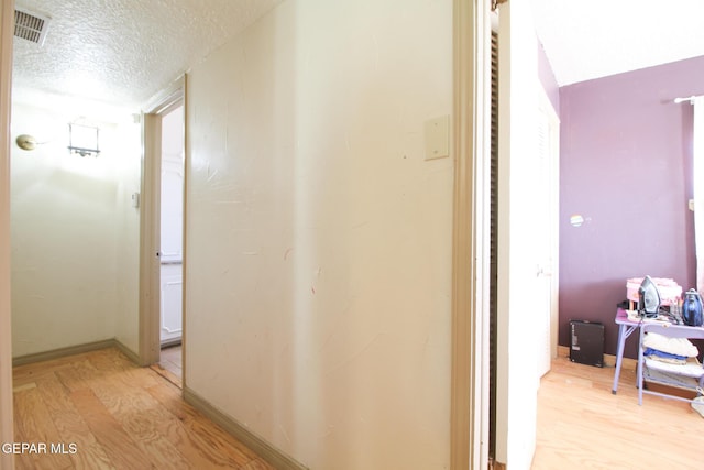 corridor with baseboards, light wood-style floors, visible vents, and a textured ceiling