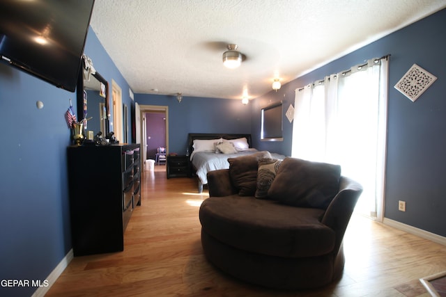 bedroom featuring light wood finished floors, a textured ceiling, and baseboards