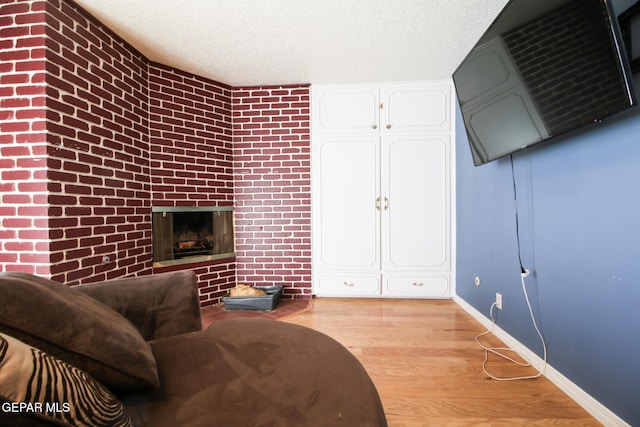 living room featuring a large fireplace, light wood-style floors, baseboards, and a textured ceiling