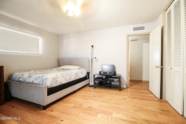 bedroom featuring a ceiling fan, visible vents, light wood-style floors, a closet, and a textured ceiling