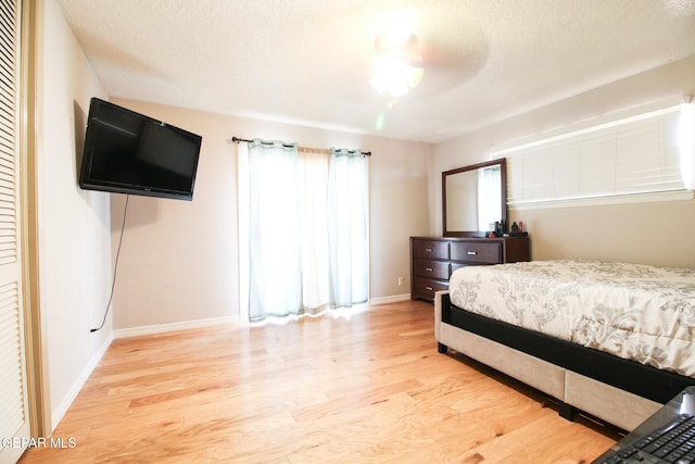 bedroom featuring light wood-style flooring, baseboards, and a textured ceiling