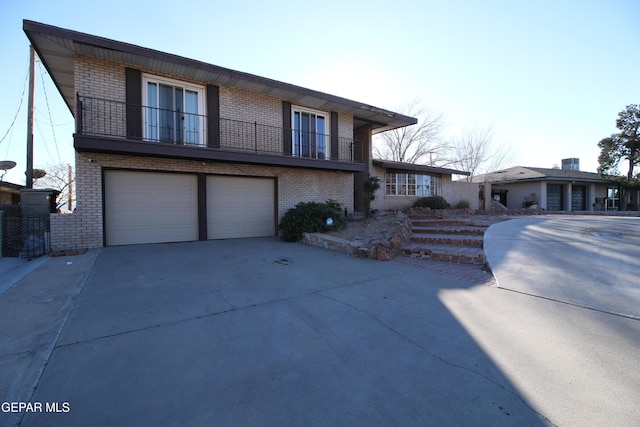 view of front of house with a balcony, a garage, brick siding, and driveway