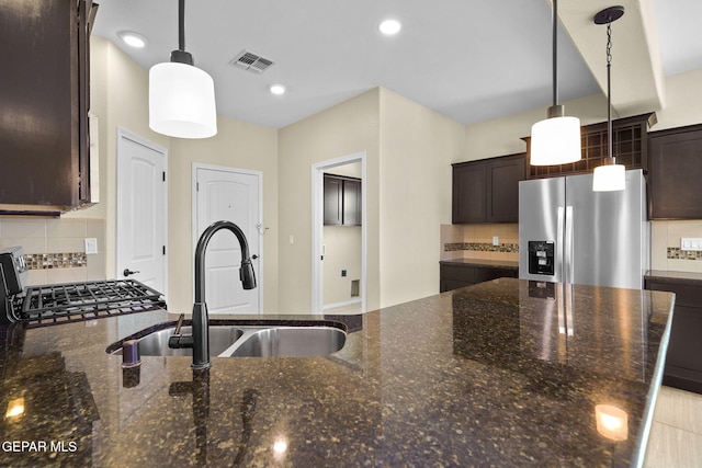 kitchen featuring visible vents, dark brown cabinetry, dark stone counters, stainless steel refrigerator with ice dispenser, and a sink