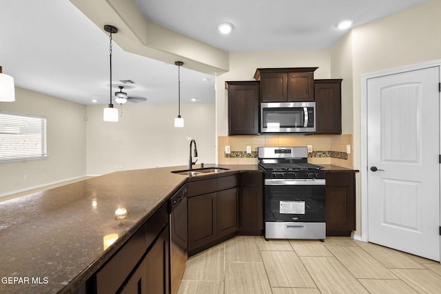 kitchen with a sink, backsplash, stainless steel appliances, dark stone counters, and dark brown cabinets