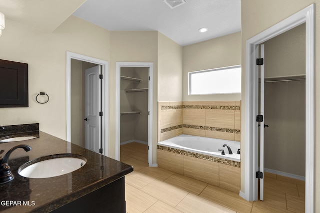 bathroom with double vanity, a spacious closet, a bath, and a sink