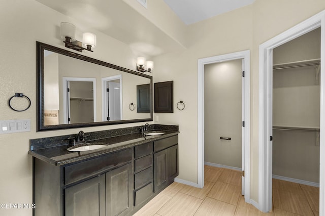 full bath featuring double vanity, a spacious closet, baseboards, and a sink