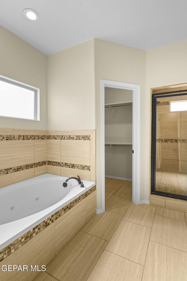 full bathroom featuring baseboards, a jetted tub, a shower stall, and a spacious closet