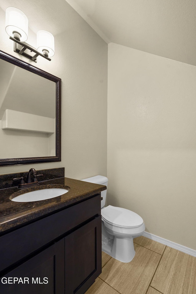 half bathroom with baseboards, toilet, wood finished floors, and vanity