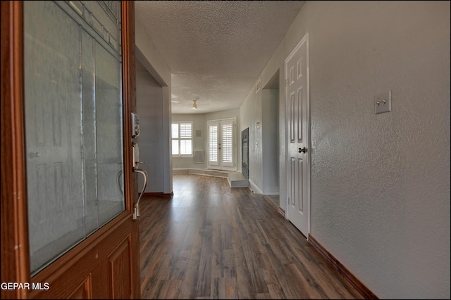 corridor with a textured wall, baseboards, dark wood-type flooring, and a textured ceiling