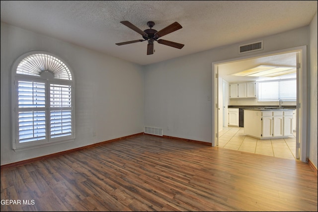 empty room with visible vents, a textured ceiling, ceiling fan, and light wood finished floors