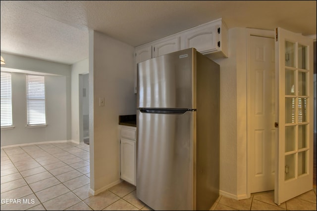 kitchen with white cabinets, light tile patterned floors, freestanding refrigerator, and a textured ceiling