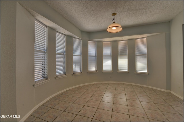 spare room featuring light tile patterned floors, baseboards, and a textured ceiling