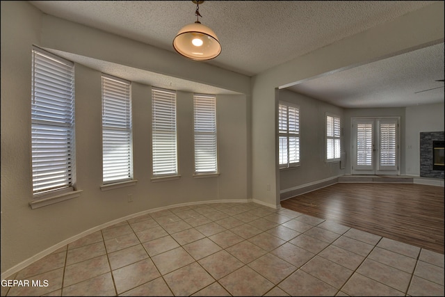 unfurnished room featuring light tile patterned floors, a fireplace, a textured ceiling, and baseboards