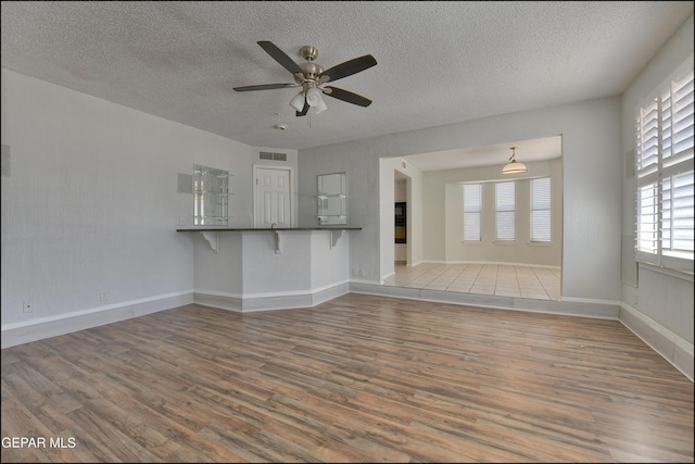 unfurnished living room with visible vents, baseboards, ceiling fan, wood finished floors, and a textured ceiling