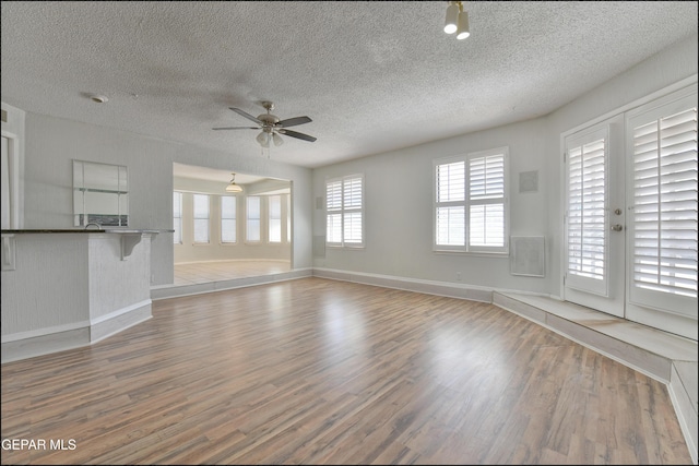 unfurnished living room featuring ceiling fan, baseboards, a textured ceiling, and wood finished floors