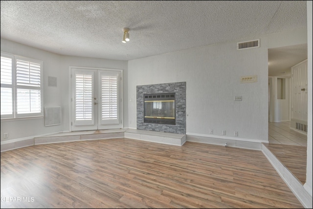 unfurnished living room with visible vents, baseboards, wood finished floors, a glass covered fireplace, and a textured ceiling