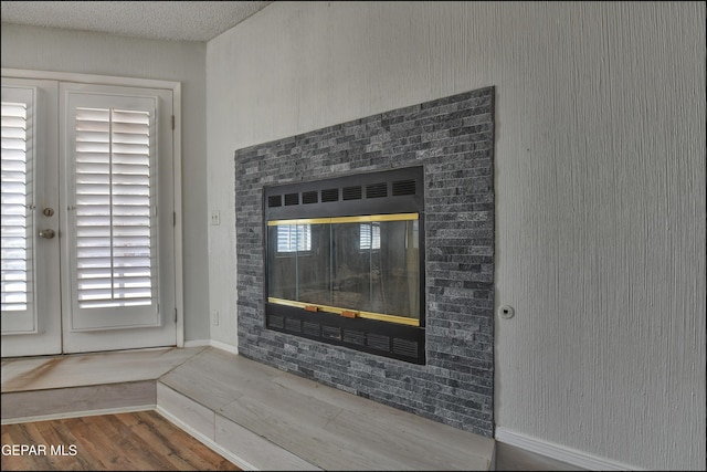 room details with a glass covered fireplace, baseboards, a textured ceiling, and wood finished floors