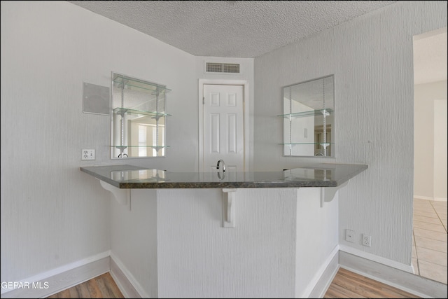 kitchen featuring visible vents, baseboards, a breakfast bar, wood finished floors, and a textured ceiling