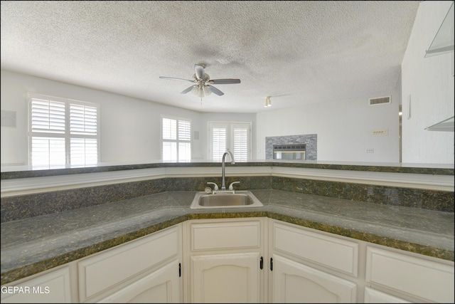 kitchen featuring visible vents, ceiling fan, a sink, white cabinets, and dark countertops