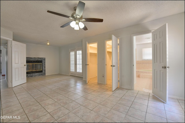 unfurnished living room featuring a stone fireplace, light tile patterned floors, a ceiling fan, and a textured ceiling