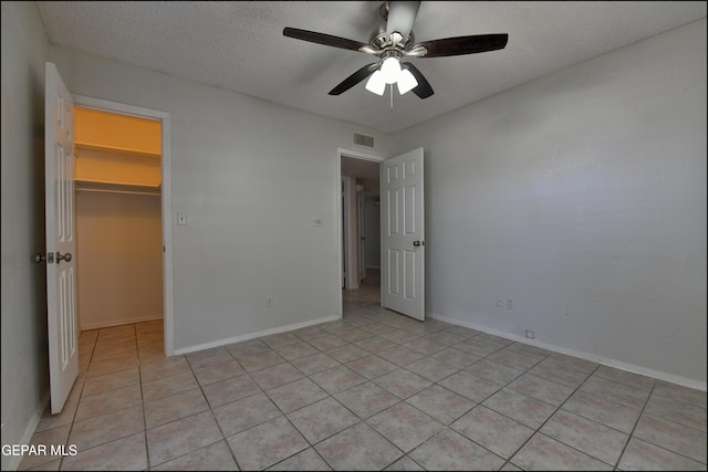 unfurnished bedroom featuring visible vents, a walk in closet, a textured ceiling, a closet, and light tile patterned flooring