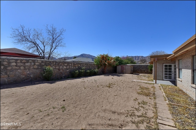 view of yard featuring a fenced backyard, a mountain view, a storage shed, and an outdoor structure