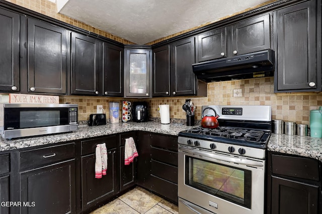 kitchen featuring under cabinet range hood, light tile patterned flooring, stainless steel appliances, and tasteful backsplash