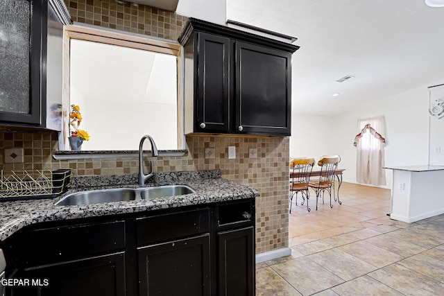 kitchen with tasteful backsplash, dark cabinets, light tile patterned floors, and a sink