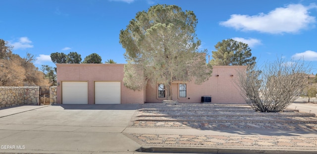 pueblo-style house with cooling unit, fence, driveway, an attached garage, and stucco siding