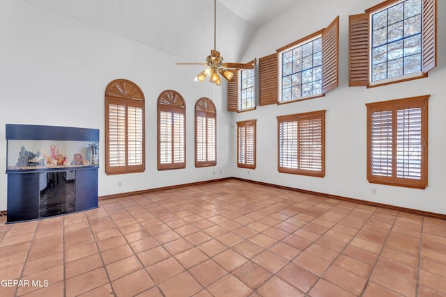 unfurnished living room with a wealth of natural light, baseboards, high vaulted ceiling, and ceiling fan