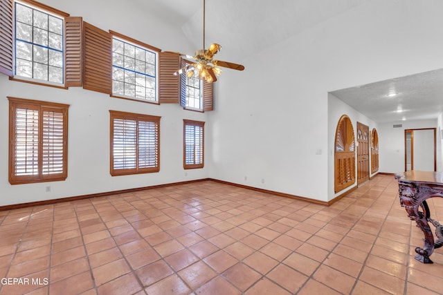 unfurnished living room featuring visible vents, baseboards, light tile patterned flooring, ceiling fan, and a towering ceiling