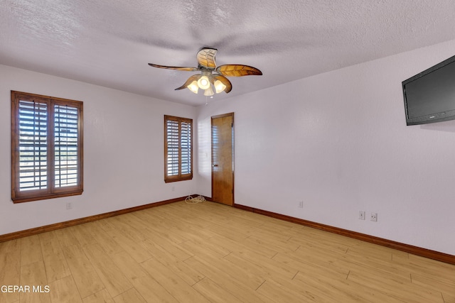 spare room with baseboards, a healthy amount of sunlight, light wood-style floors, and a textured ceiling