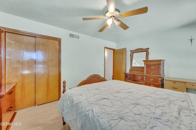 bedroom featuring visible vents, a textured ceiling, a closet, light wood-style floors, and ceiling fan