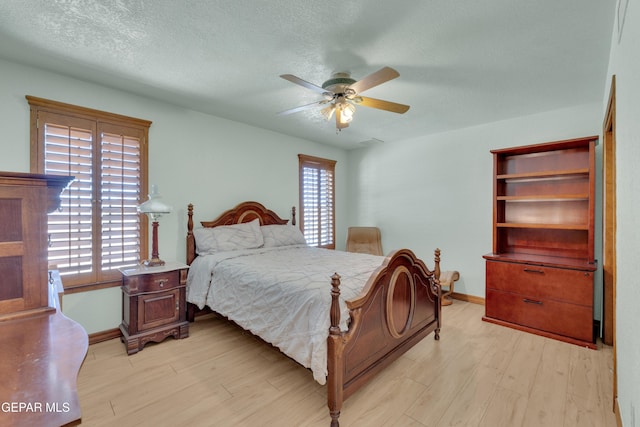 bedroom featuring ceiling fan, a textured ceiling, light wood-type flooring, and baseboards