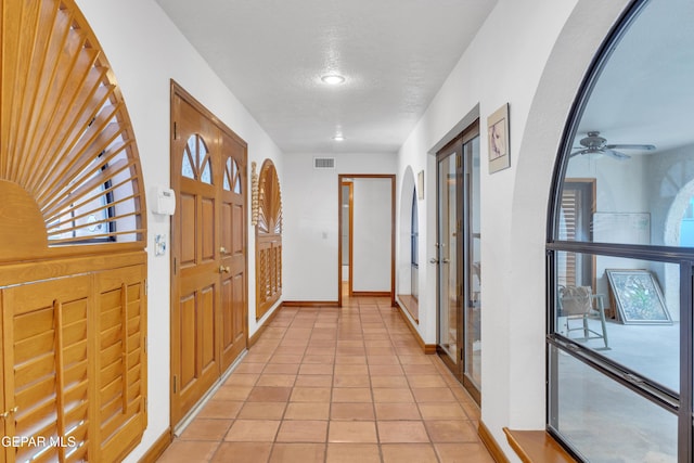 hallway featuring arched walkways, visible vents, baseboards, and light tile patterned floors